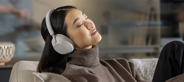 Sony WH-1000XM5 on the head of a woman sitting on a couch listening to music